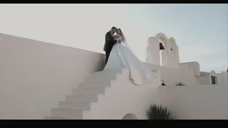 A bride and groom embrace on white architectural steps beneath a pale sky