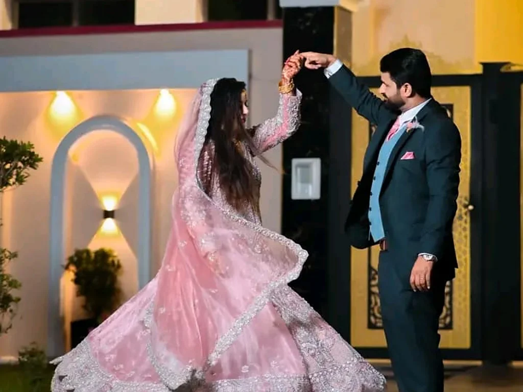 A bride and groom dance together, her lehenga skirt flaring, outside an illuminated venue at night